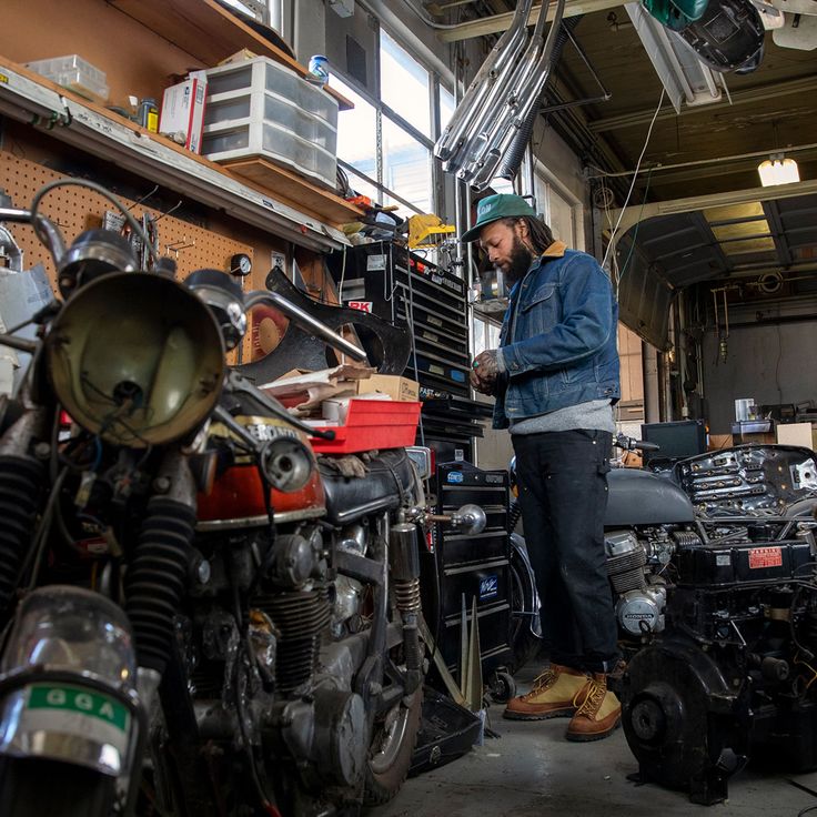 a man standing next to a motorcycle in a room filled with other motorcycles and parts