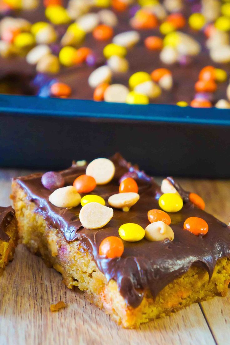 a piece of cake with chocolate frosting and candy corn on top, next to a tray of cookies