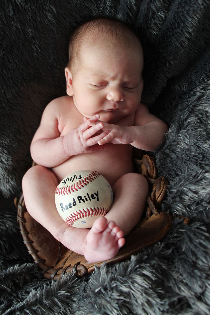 a baby is sitting in a baseball mitt with his hands on his chest and eyes closed