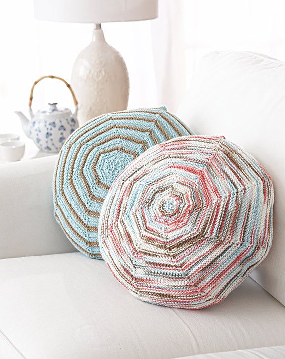 two crocheted pillows sitting on top of a white couch next to a lamp