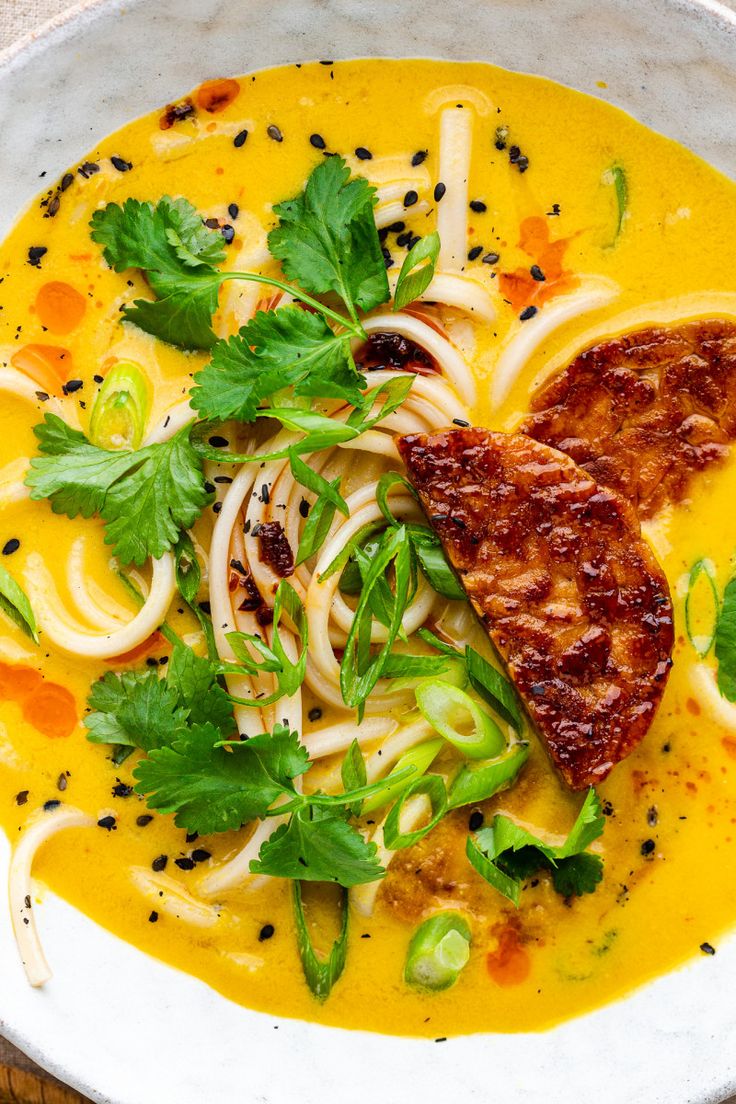 a white bowl filled with soup and vegetables on top of a table next to a spoon