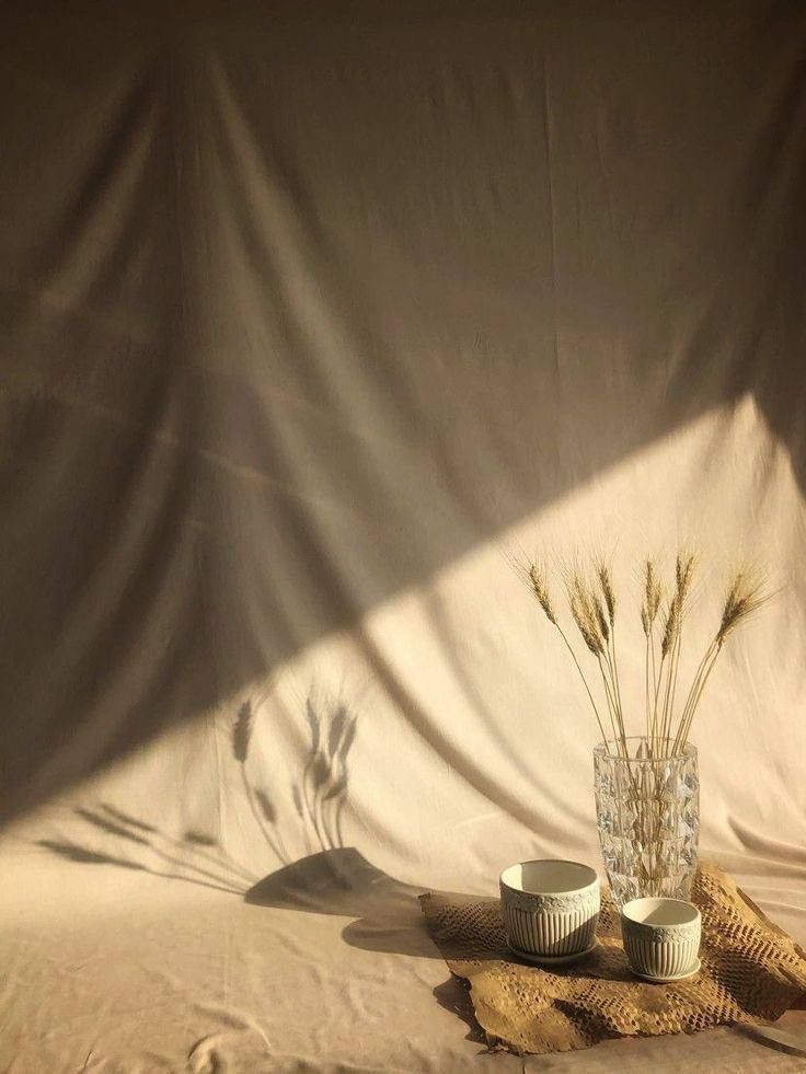 two white bowls sitting on top of a bed next to a vase filled with flowers