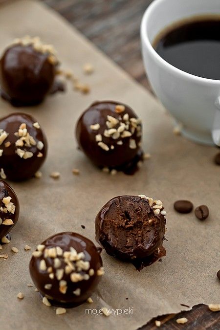 some chocolate balls are on a piece of parchment paper next to a cup of coffee