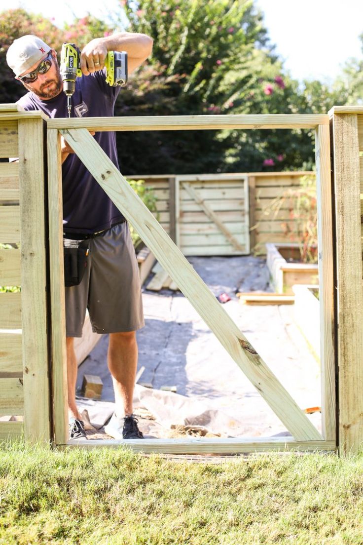 a man is working on an outdoor wooden gate in the yard with his hands up