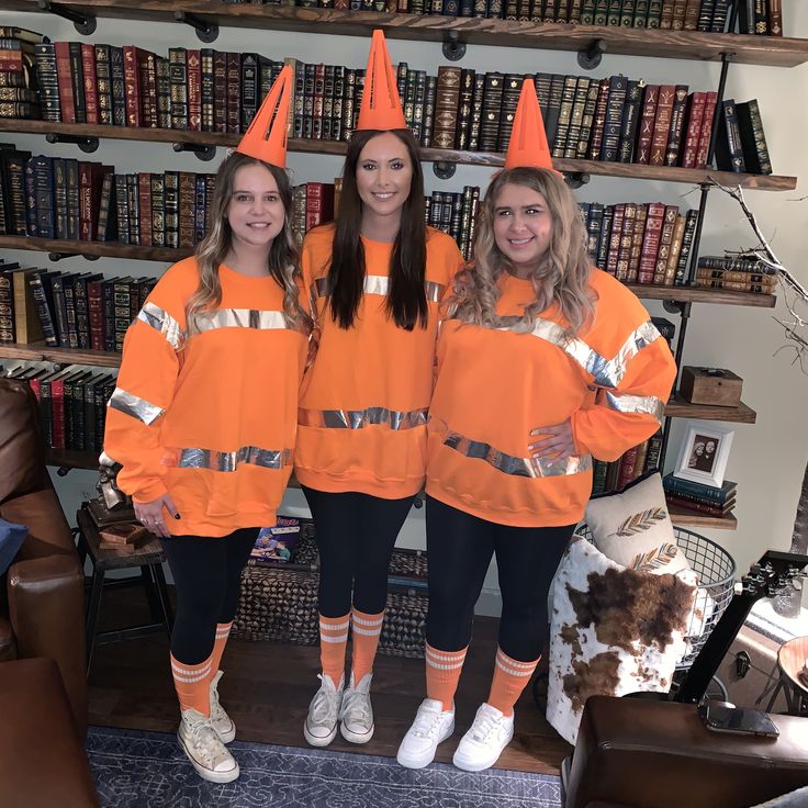 three girls in orange sweatshirts standing next to bookshelves and shelves full of books