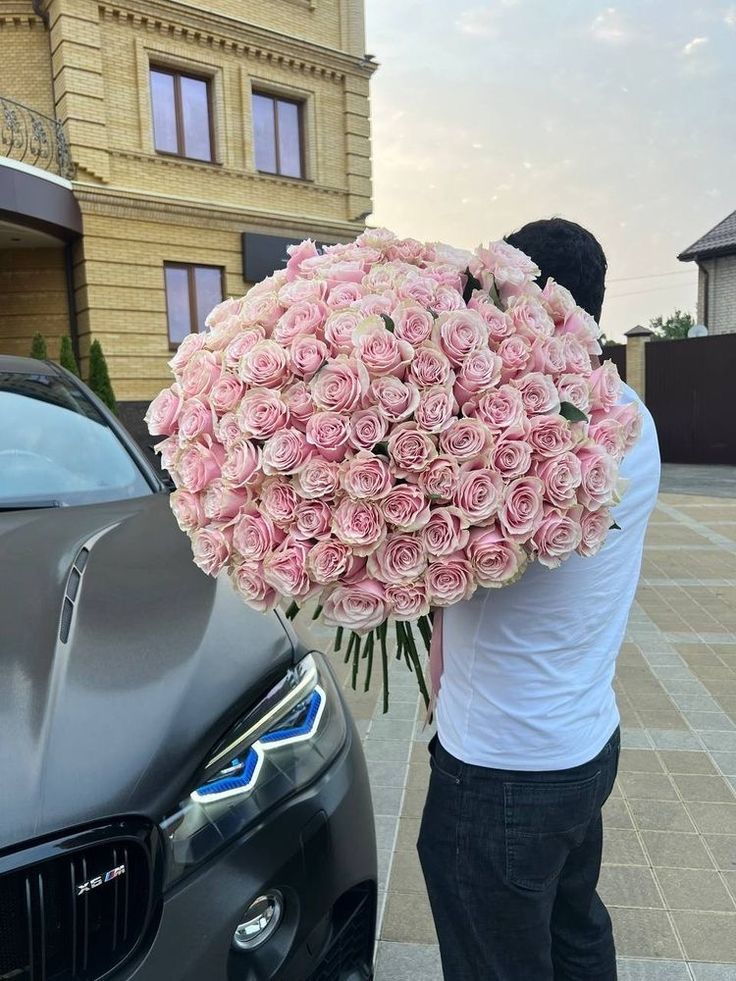 a man is holding a large bouquet of pink roses in front of a black car