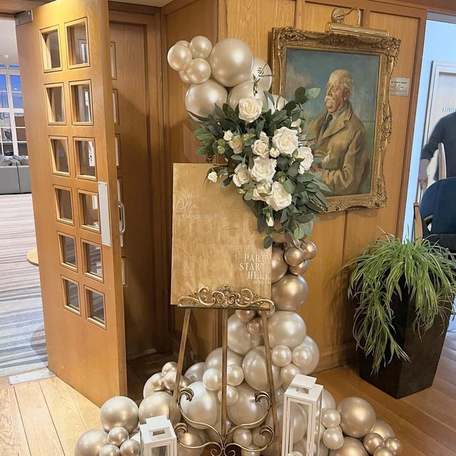 an arrangement of silver and white ornaments on a table in front of a door with a painting