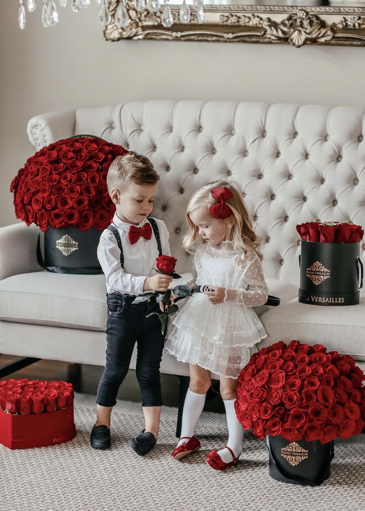 two young children standing next to each other in front of red roses on a couch