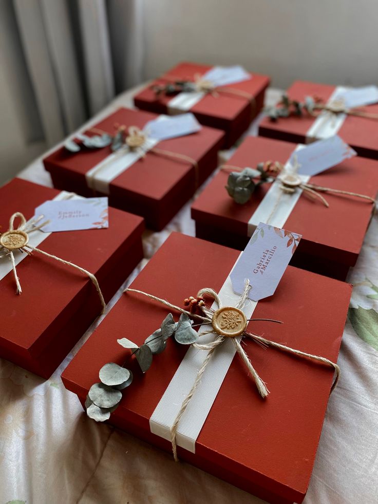 several red boxes with white ribbons and tags tied to them on top of a bed