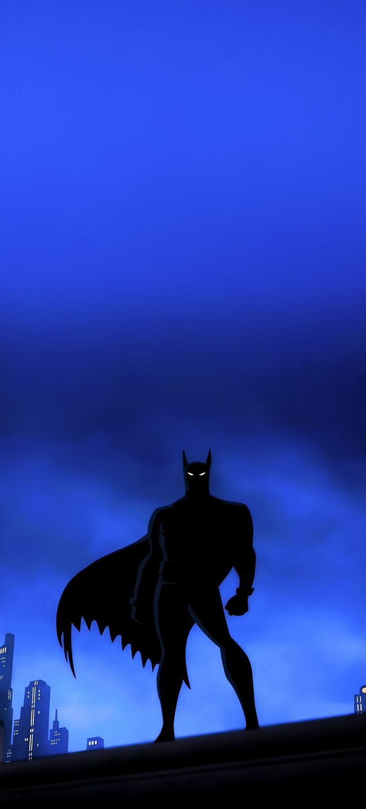 a batman silhouetted against a blue sky with buildings in the background