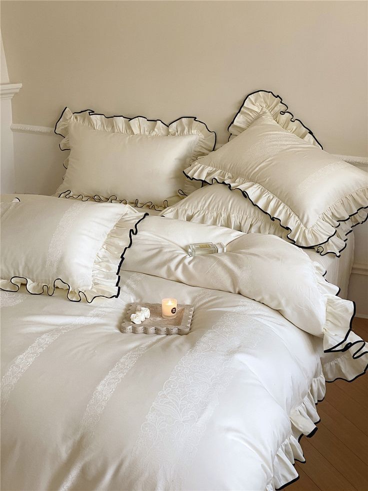 a white bed topped with pillows next to a night stand and candle on top of it