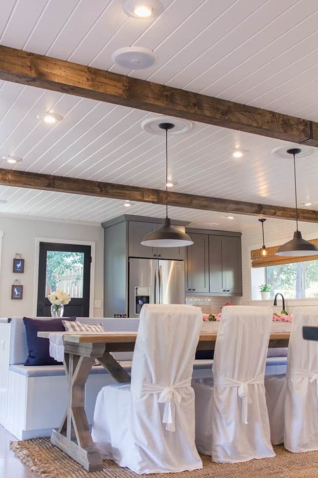 a dining room table and chairs covered in white cloths with lights hanging from the ceiling