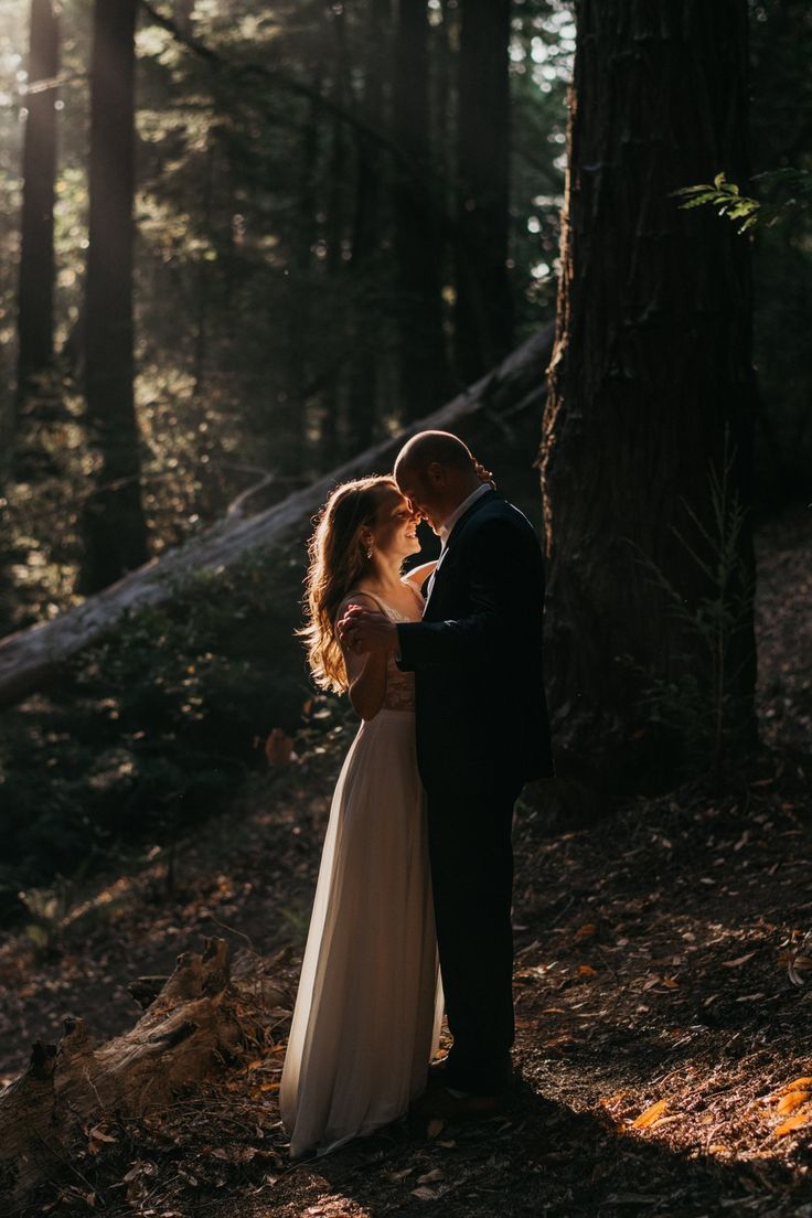 a bride and groom standing in the woods