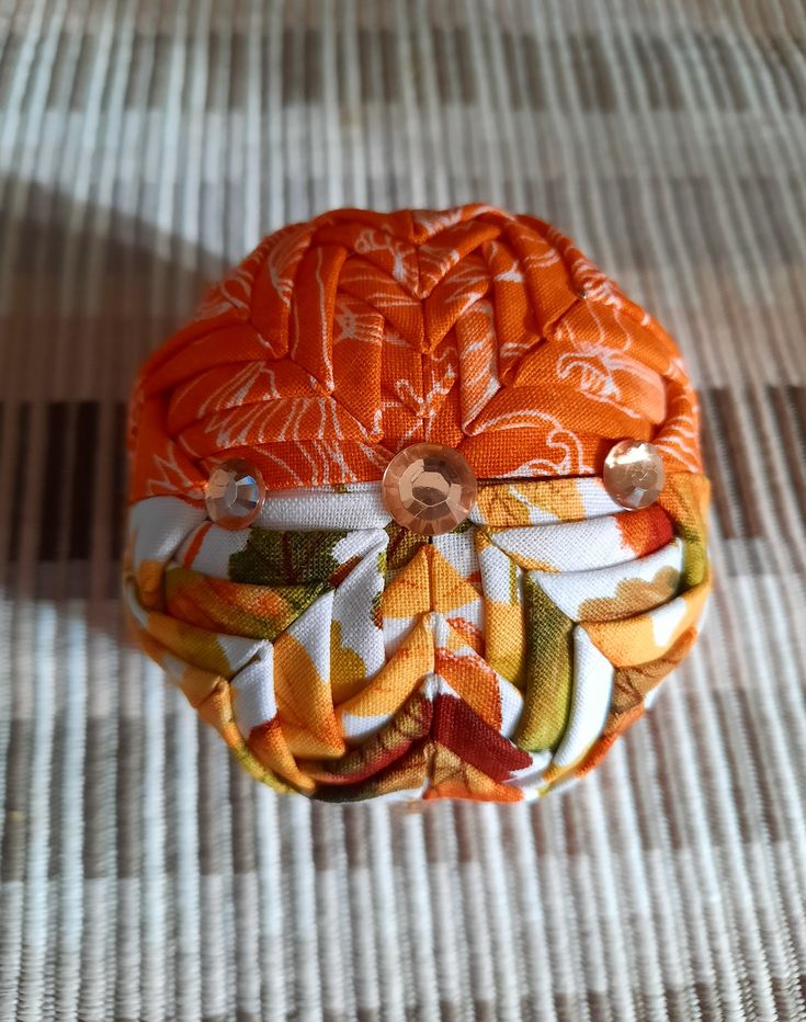 an orange and white fabric covered object sitting on top of a striped cloth tablecloth