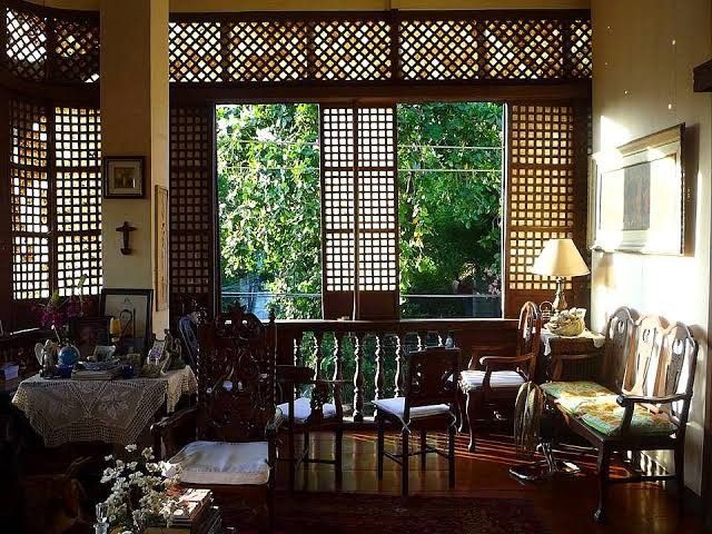 a living room filled with lots of furniture next to a window covered in latticed screens