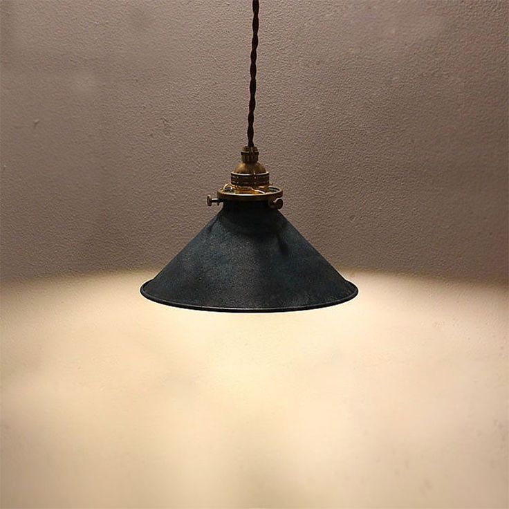 a light hanging from a ceiling with a white wall behind it and a black cord