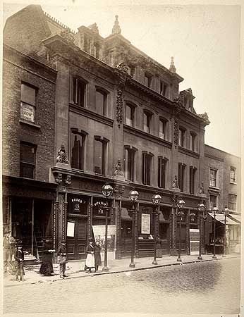 an old black and white photo of people standing on the sidewalk in front of buildings