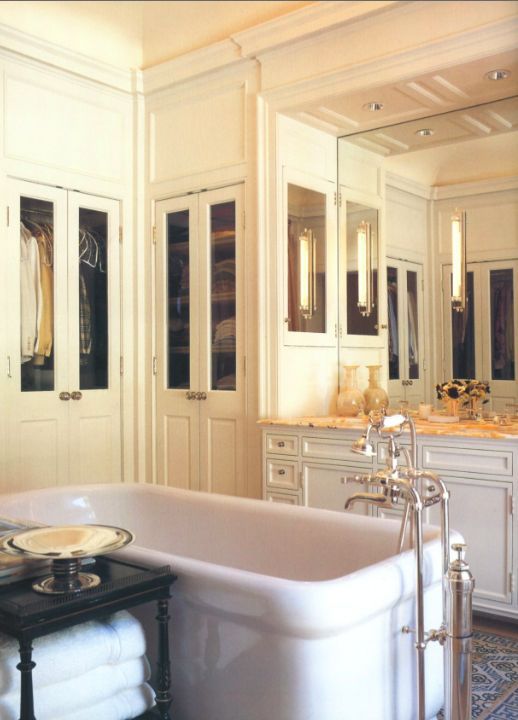 a bath tub sitting next to a sink in a bathroom under a mirror and cabinets