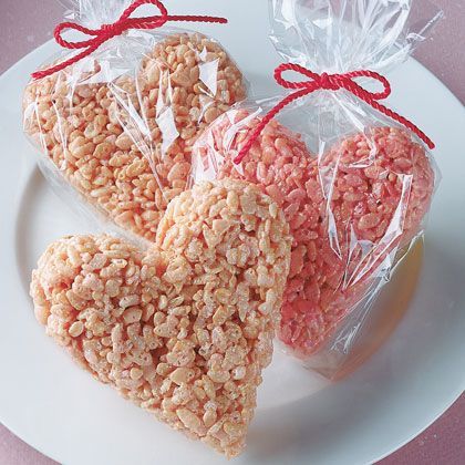 two heart shaped rice krispy treats on a white plate with red ribbon tied around them