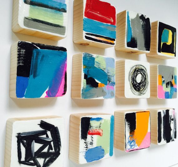 several different types of abstract paintings are displayed on a white wall with wooden trays