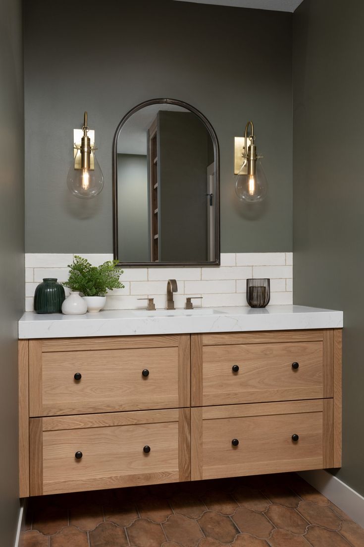 a bathroom vanity with two sinks and large mirror above it, in front of a gray wall