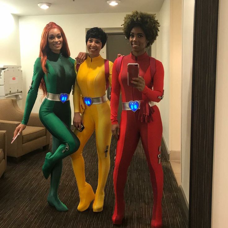 three women in costumes standing next to each other holding cell phones and smiling at the camera