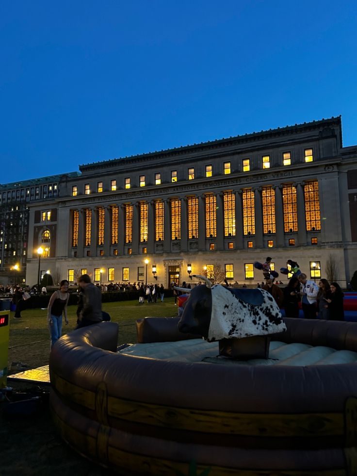 an inflatable cow is on the lawn at night with people standing around it