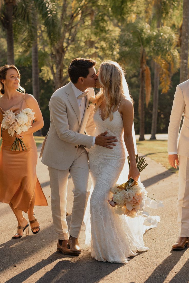 a bride and groom kiss as they walk down the street with other people behind them