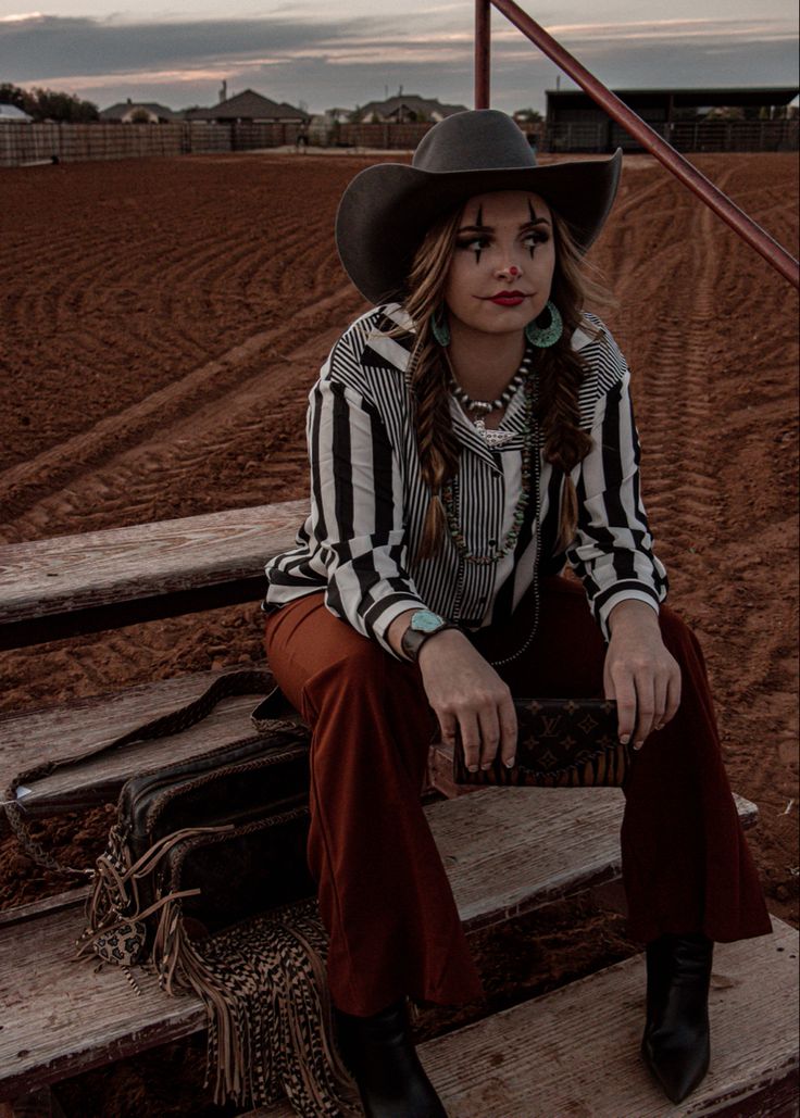 a woman wearing a cowboy hat sitting on some steps in front of a dirt field