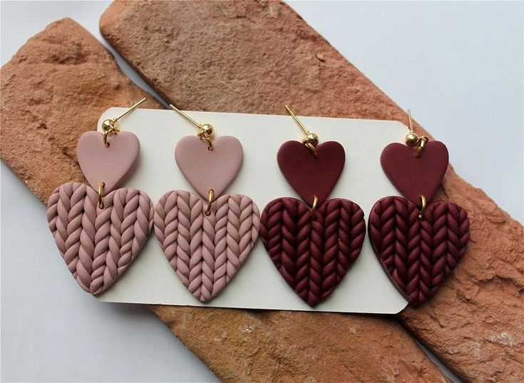 four heart shaped earrings on top of a card next to some rocks and stone slabs