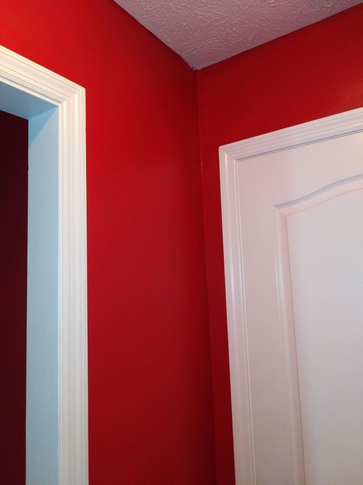 an empty bathroom with red walls and white trim on the door, toilet paper dispenser next to it