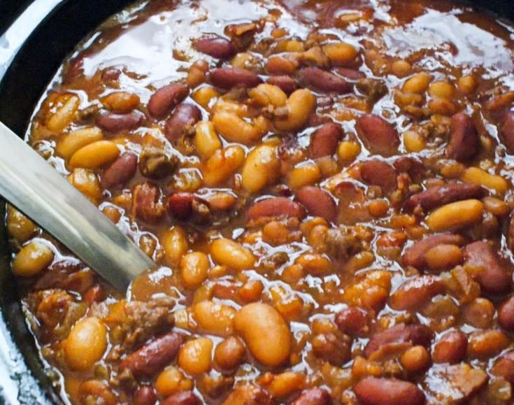 a pot full of beans and meat with a spoon in it