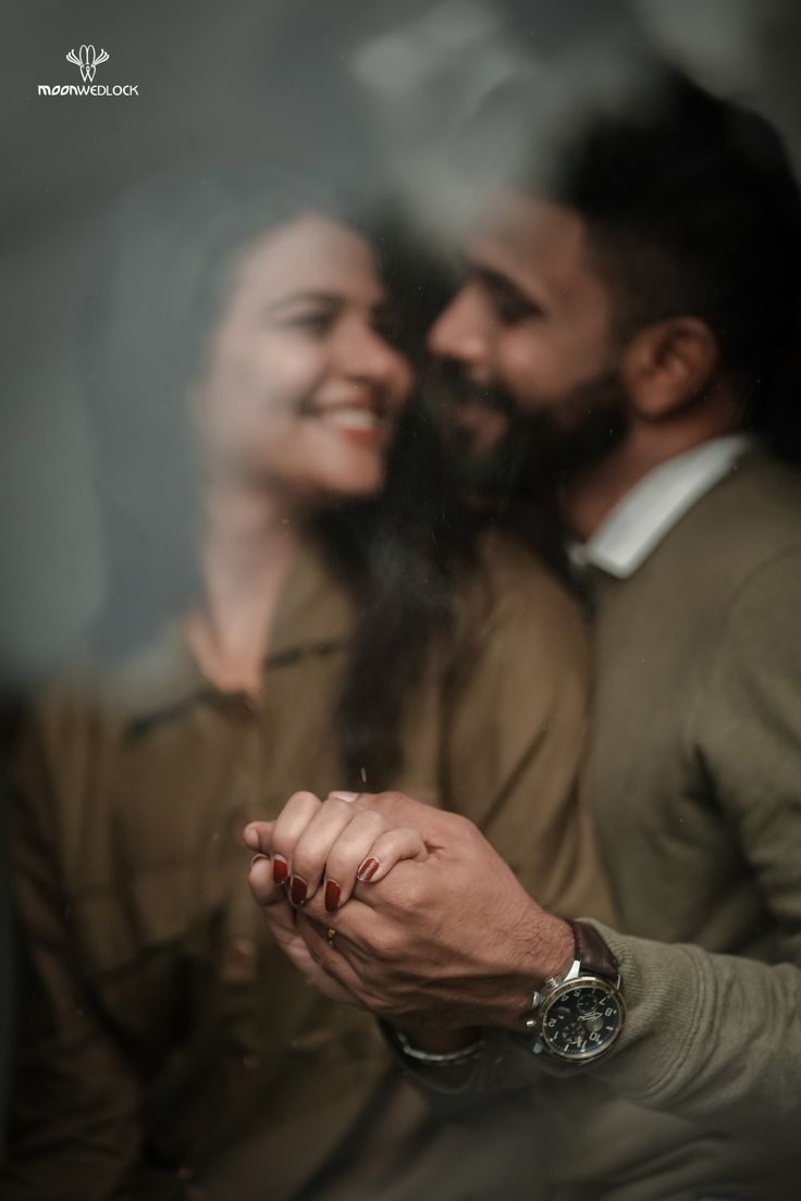 a man and woman holding each other's hand while looking at the camera through a window