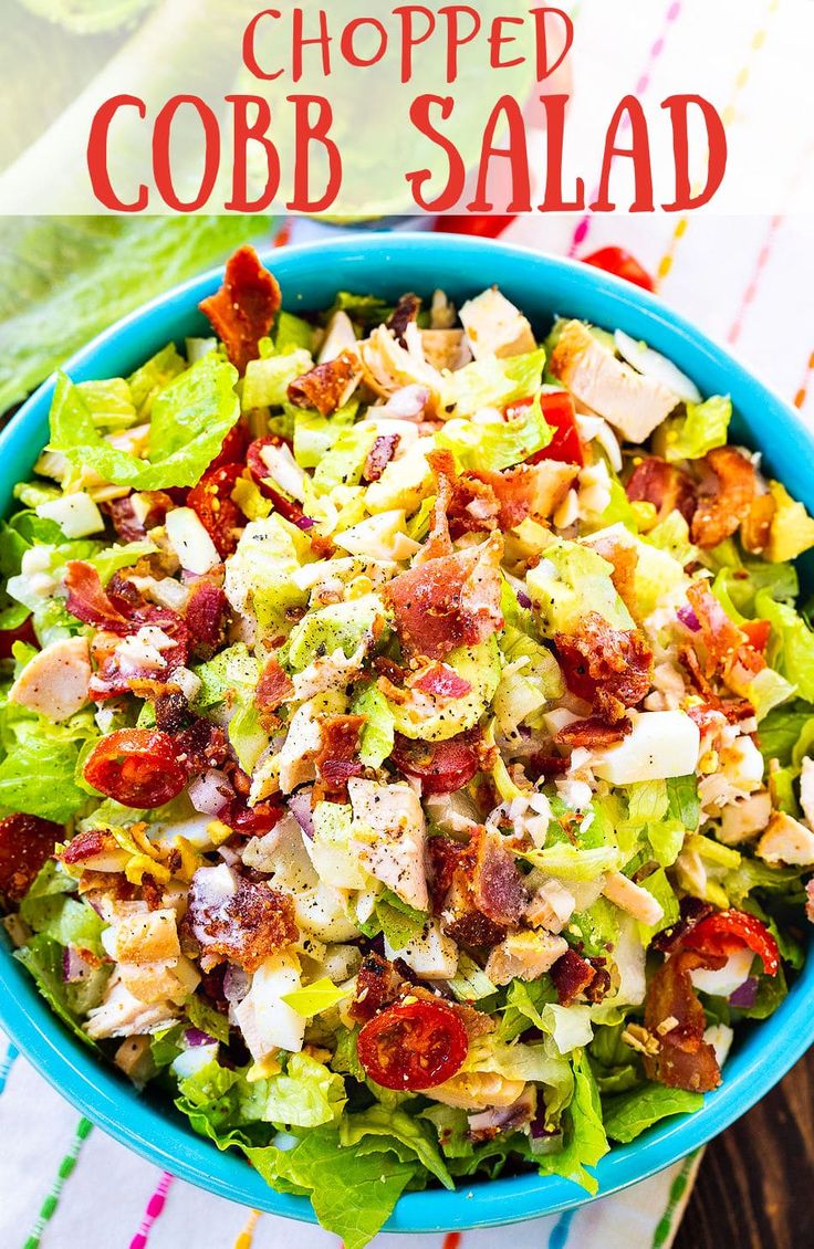 a salad in a blue bowl with bacon and lettuce on top, sitting on a colorful table cloth