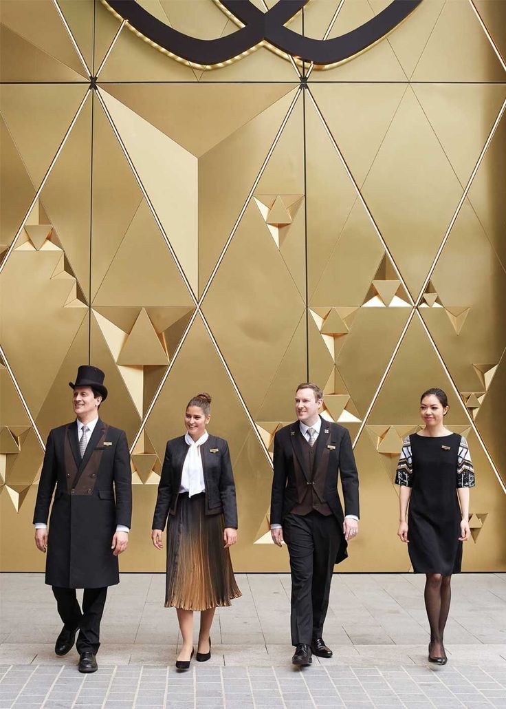 three men and two women walking in front of a gold wall with geometric shapes on it