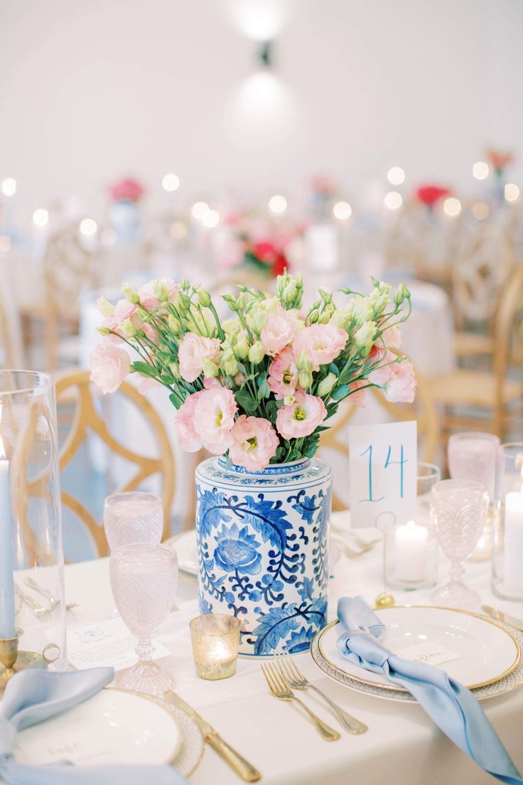 a blue and white vase filled with pink flowers on top of a table next to silverware