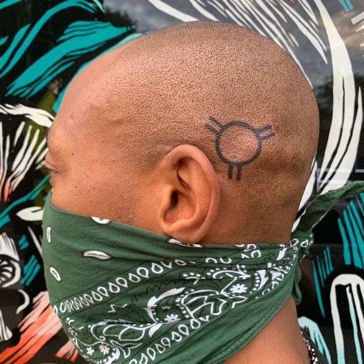 a bald man with a bandana on his head and an eye tattoo on his forehead