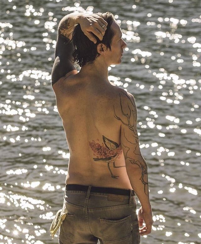 a man with tattoos on his back standing next to the water