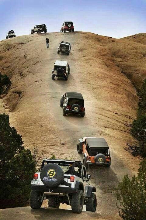 several jeeps driving up a hill with people standing on the side