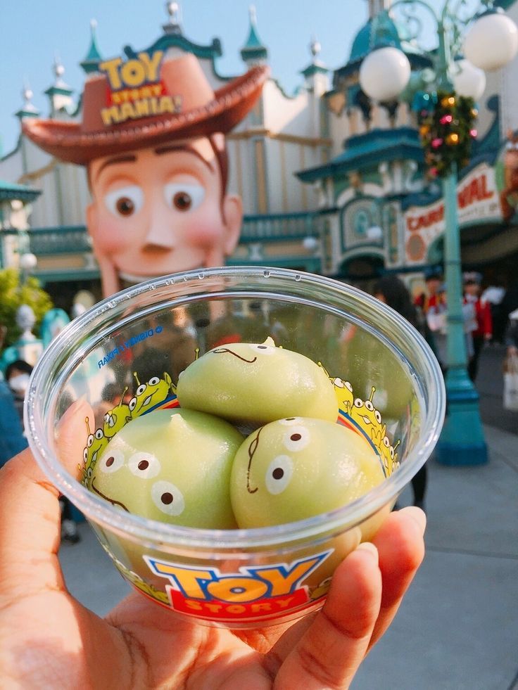 a hand holding a plastic bowl filled with green olives in front of a cartoon character