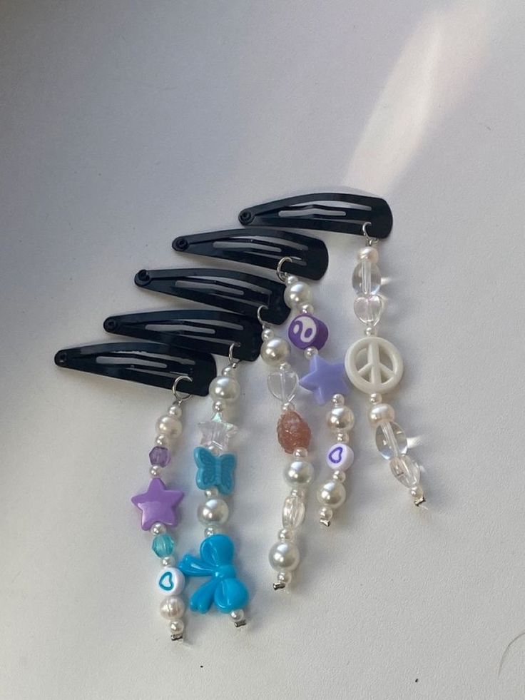 four hair clips with different colored beads and charms hanging from them on a white surface