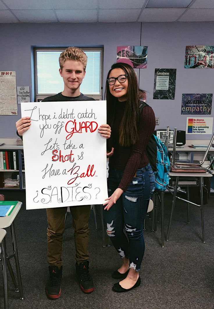 a man and woman holding up a sign in front of a classroom desk with chairs