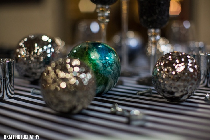 three glass balls sitting on top of a black and white table cloth next to wine glasses