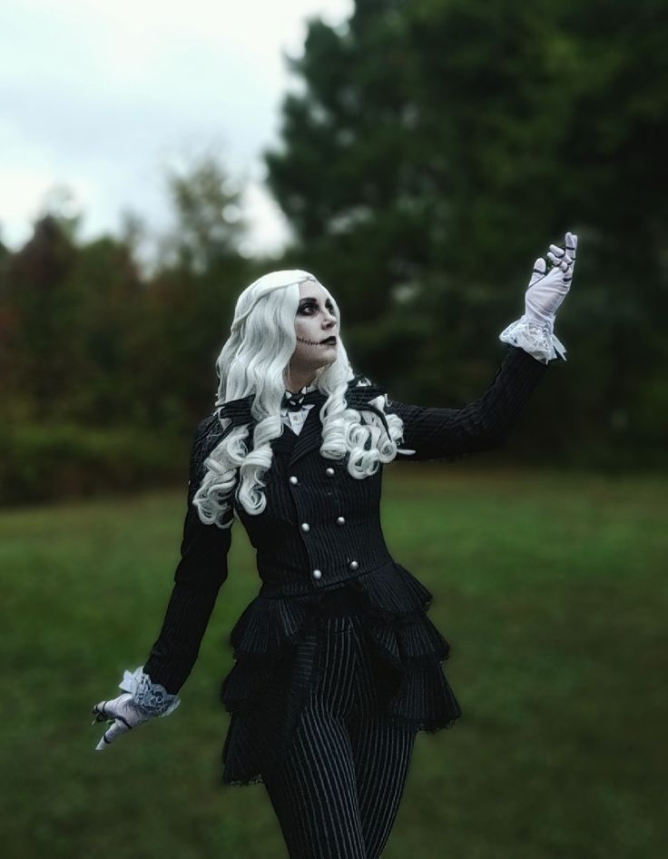 a woman dressed in black and white is walking through the grass with her hands up