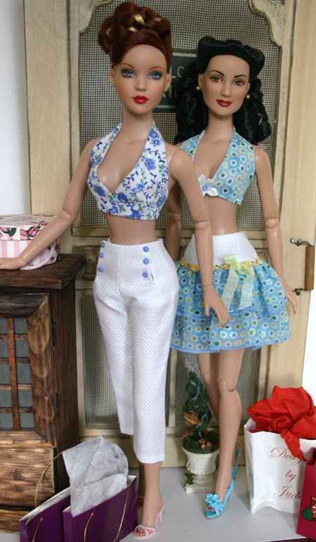 two dolls standing next to each other in front of a table with presents on it