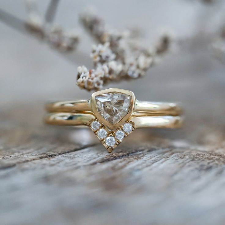 two gold rings with white diamonds on them sitting on a piece of wood next to some flowers