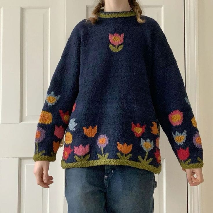 a woman standing in front of a white door wearing a sweater with flowers on it