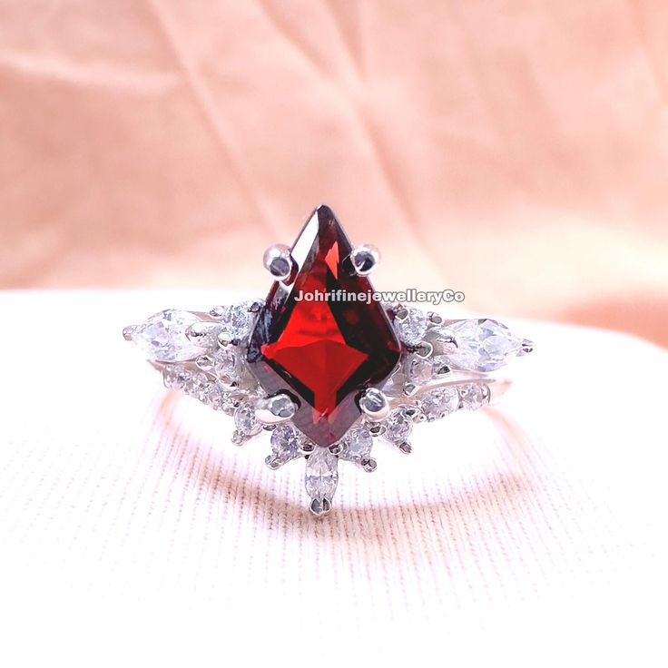 a ring with a red stone surrounded by clear crystal stones on a white cloth background