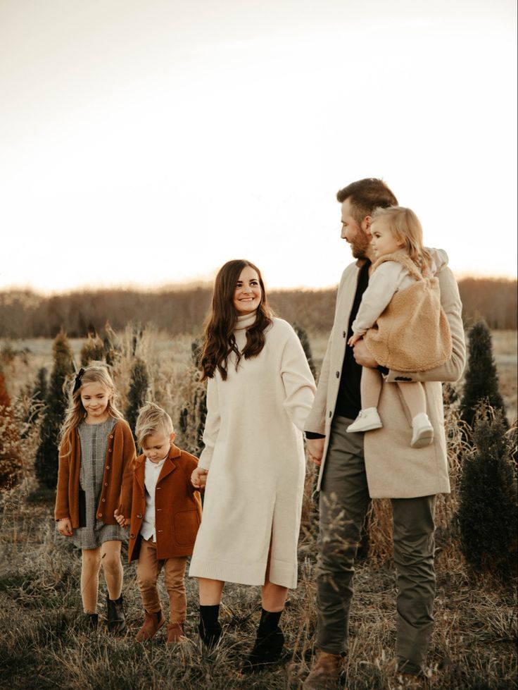 a man and woman holding hands while walking with their two children in a field at sunset