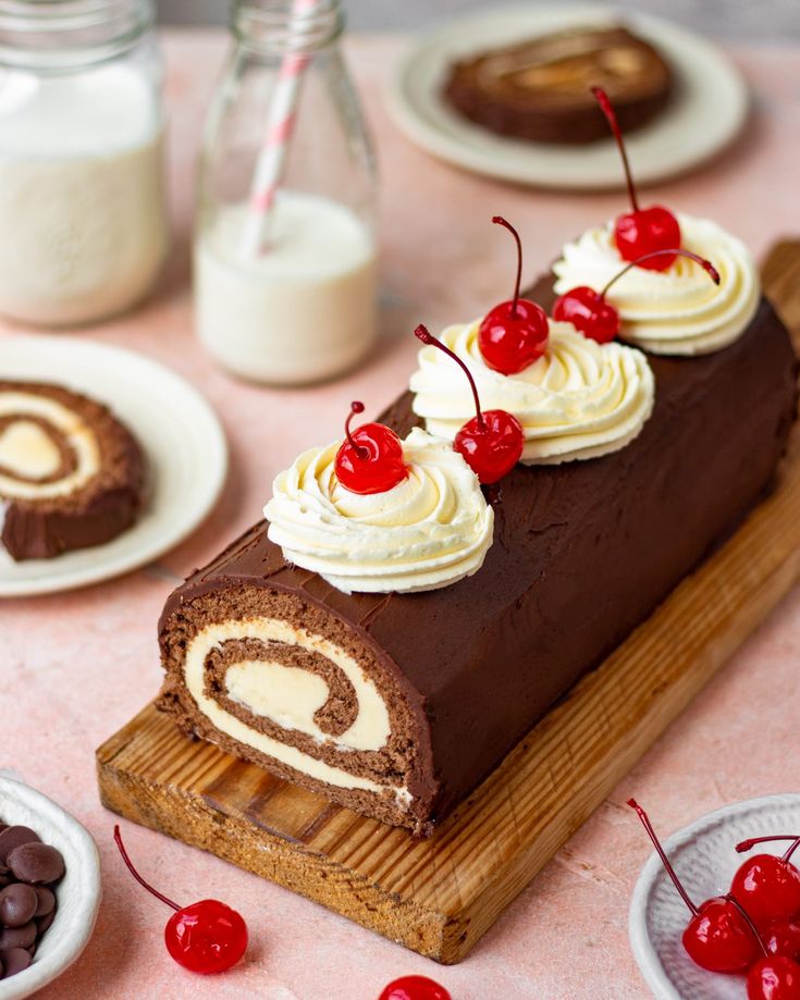 there is a chocolate roll with cream and cherries on the table next to other desserts